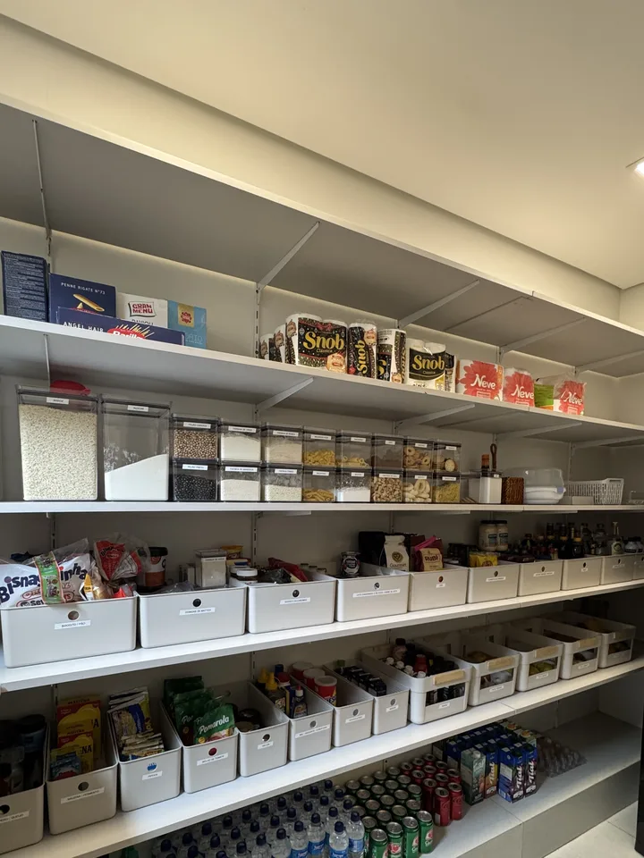 Parede de despensa com prateleiras cheias, potes transparentes de mantimentos e cestas etiquetadas por categoria