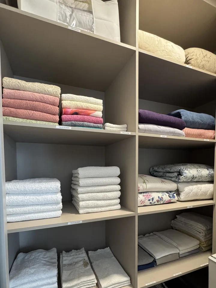 Rouparia com toalhas e roupa de cama dobradas em pilhas, cada nicho com etiqueta