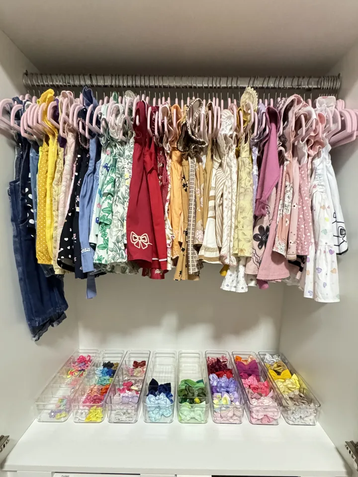 Guarda-roupa infantil com vestidos em cabides iguais e bandejas de laços separados por cor